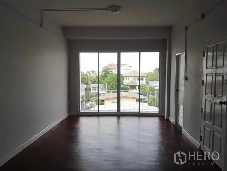 联排别墅 出租或出售在Din Daeng, Bangkok - 客厅采用落地推拉门，采光充足通向阳台与城市景观，深色木地板。