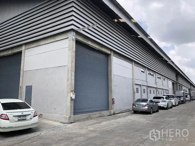 货栈 出租在Khlong Sam Wa, Bangkok - 仓库侧立面，连续装卸卷闸门，宽阔卡车通道，混凝土结构。