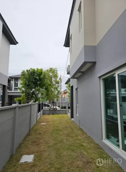 Detached House for rent in Bang Phli, Samut Prakan - Lawn running along the side of the house with boundary wall and front trees.