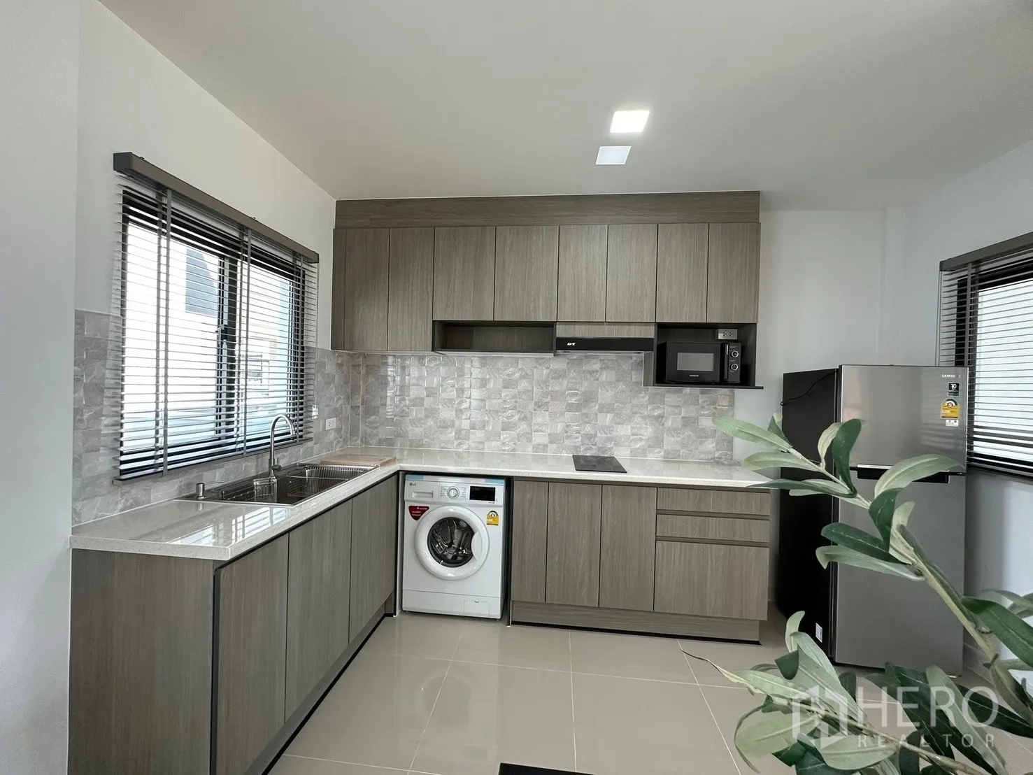 Townhouse for rent in Bang Phli, Samut Prakan - L-shaped kitchen with stone-look backsplash, sink, and a washing machine.