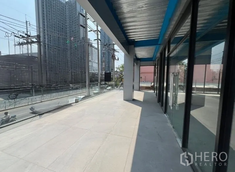 零售空间 出租在Huai Khwang, Bangkok - 带顶露台与宽阔临街面，俯瞰繁忙主干道与高楼，旁为通高玻璃店窗。