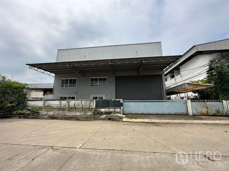 工厂 出租或出售在Bang Bua Thong, Nonthaburi - 邦武通现代工厂外观，宽阔车道、高挑雨棚与大型卷闸门。
