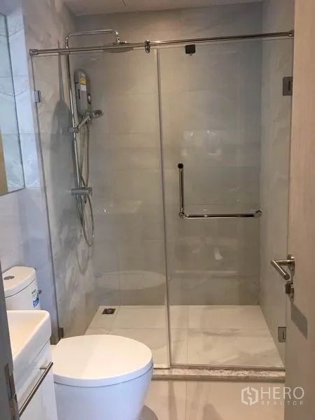 Condominium for rent in Watthana, Bangkok - Bathroom with glass-enclosed walk-in shower and white tiles.