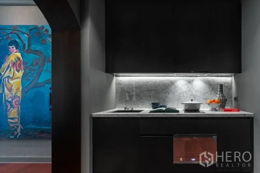 Condominium for sale in Watthana, Bangkok - Compact kitchenette with dark cabinetry and marble backsplash under task lighting.