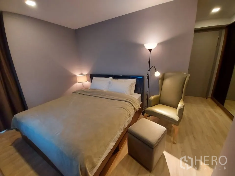 Condominium for rent in Watthana, Bangkok - Second bedroom with double bed, armchair, ottoman and warm lighting.