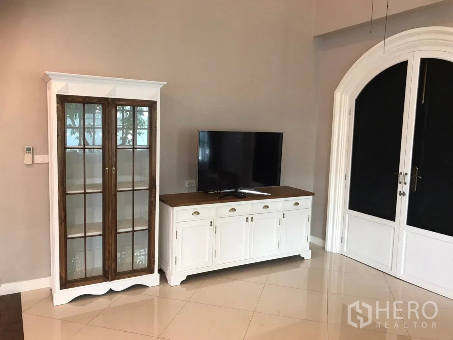 Detached House for rent in Mueang Samut Prakan, Samut Prakan - Living room corner with TV console and glass display cabinet near arched double doors.