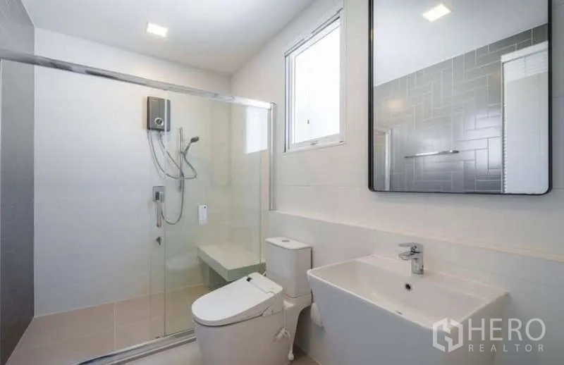 Detached House for rent in Prawet, Bangkok - Modern bathroom with glass shower enclosure, window, white vanity and toilet.