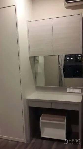 Condominium for rent in Mueang Samut Prakan, Samut Prakan - Built-in vanity with mirror and overhead cabinets beside a window showing city night views and air conditioning.