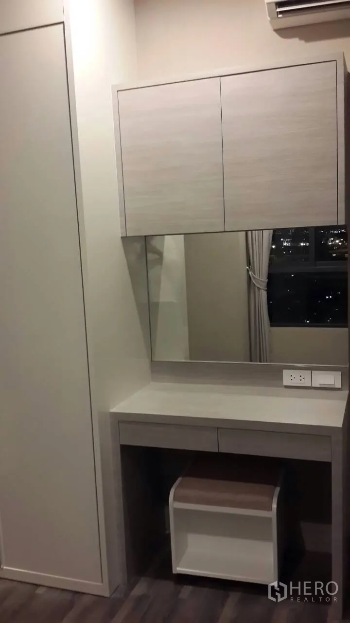 Condominium for rent in Mueang Samut Prakan, Samut Prakan - Built-in vanity with mirror and overhead cabinets beside a window showing city night views and air conditioning.