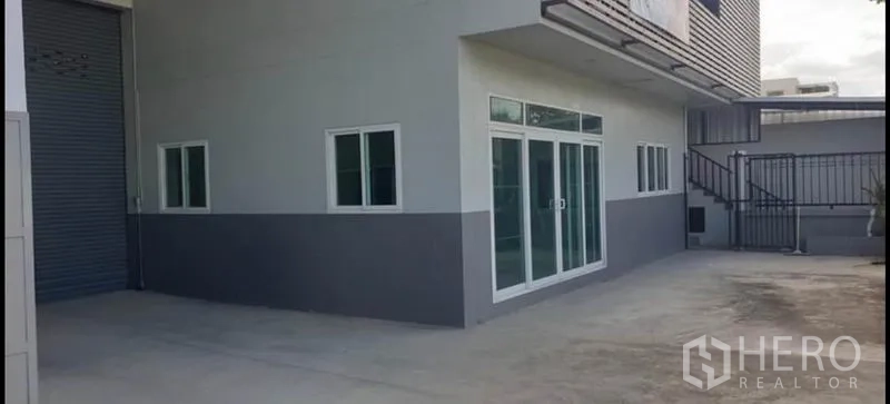 货栈 出租在Khlong Luang, Pathum Thani - 侧院带卷帘门、玻璃办公室入口与混凝土装卸区。