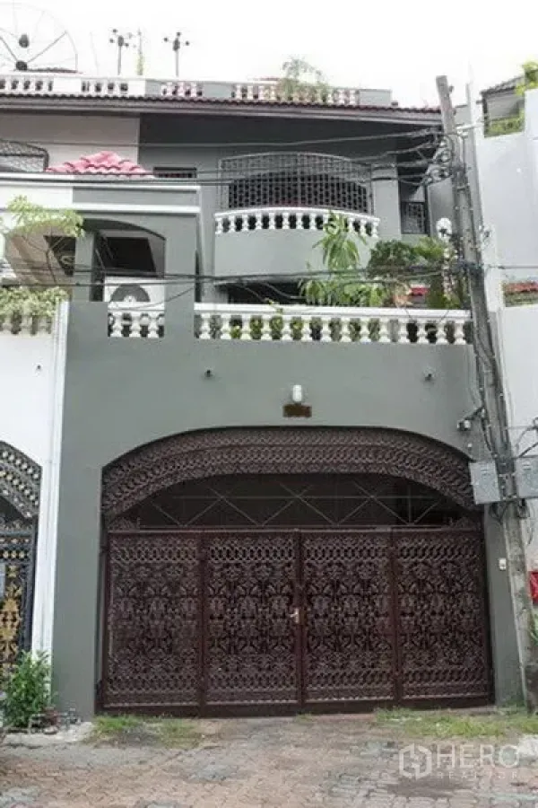 Townhouse for rent in Khlong Toei, Bangkok - Three-storey townhouse facade with ornate metal gate, arched entry and balcony planters.