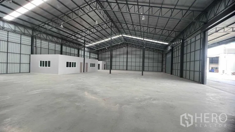 Warehouse for rent in Pathum Thani - Open warehouse interior showing skylight panels, two built-in office rooms and wide loading door openings.