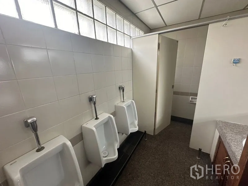 สำนักงาน ให้เช่า - ห้องน้ำชายในอาคารสำนักงาน มีโถปัสสาวะติดผนังสามจุด ผนังปูกระเบื้องและห้องส้วมแยก พร้อมช่องแสงบล็อกแก้ว