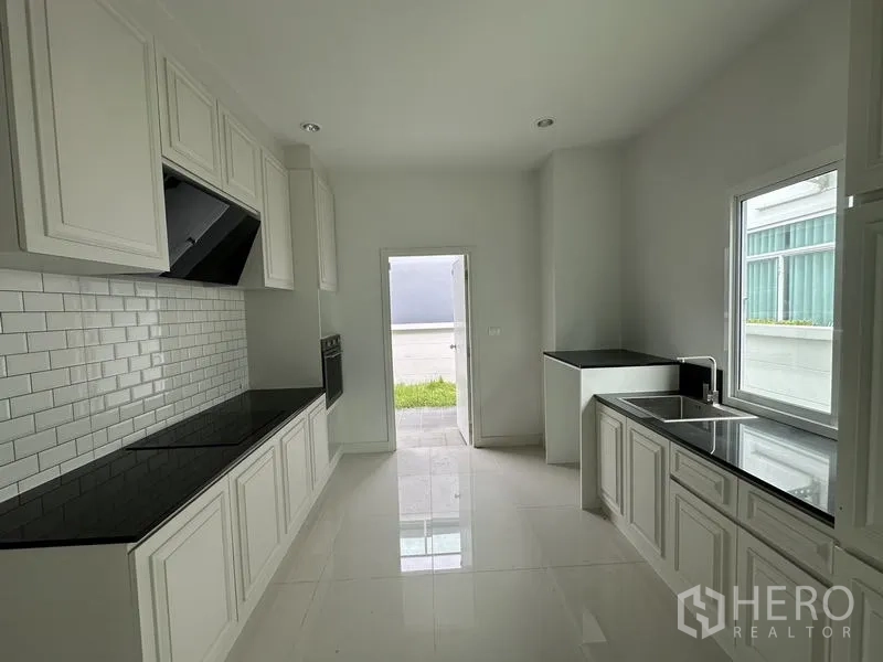 บ้าน ขายในLam Luk Ka, Pathum Thani - ครัวปิดตู้สีขาว ผนังอิฐซับเวย์ และท็อปหินสีดำ
