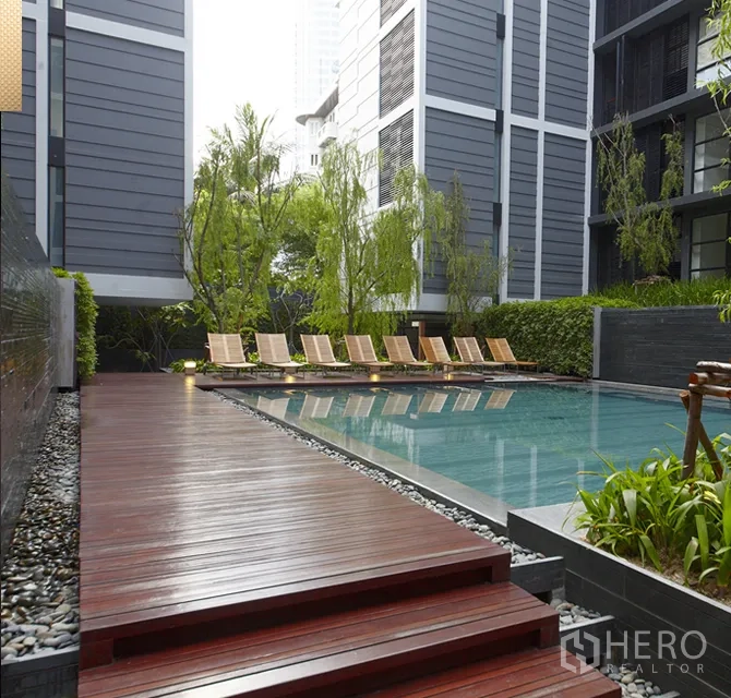 Condominium for rent in Watthana, Bangkok - Condominium outdoor swimming pool with timber deck, sun loungers and lush greenery.