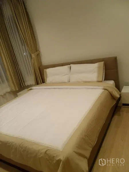 คอนโด ให้เช่าในKhlong Toei, Bangkok - ห้องนอนเตียงคู่ ผ้าปูโทนเบจ โต๊ะข้างเตียง และหน้าต่างบานใหญ่พร้อมผ้าม่าน