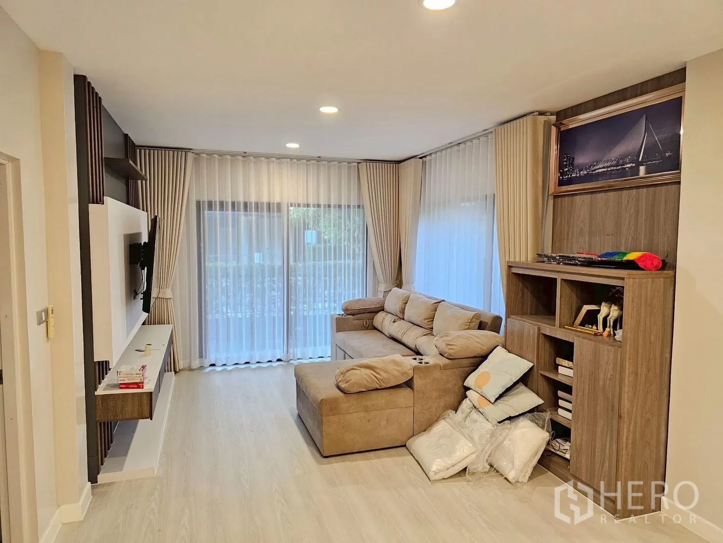 Detached House for sale in Bang Phli, Samut Prakan - Bright living room with L-shaped sofa, built-in TV wall and shelving, and floor-to-ceiling curtains to the garden.
