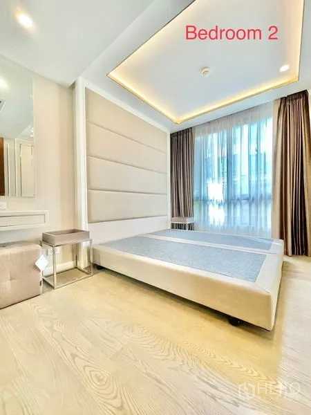 Condominium for sale in Huai Khwang, Bangkok - Second bedroom with large window, padded headboard and sheer curtains.