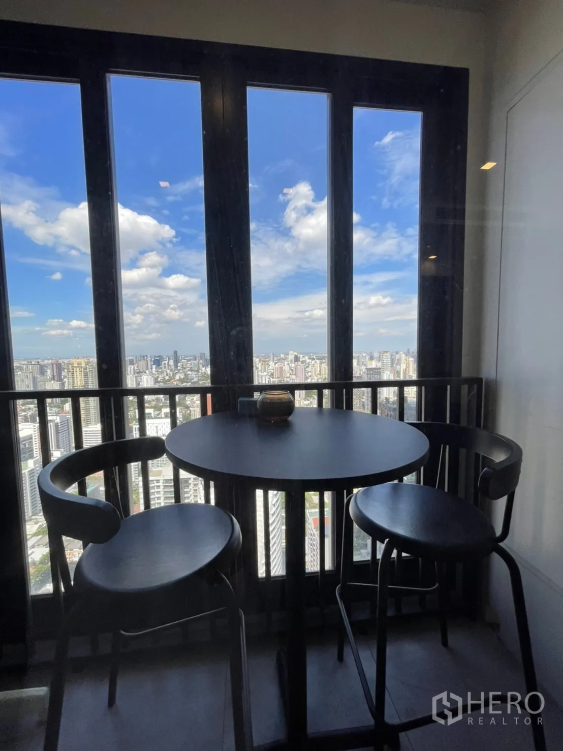 公寓 for rent in Watthana, Bangkok - 封闭阳台设圆桌与高脚椅，俯瞰城市天际线。