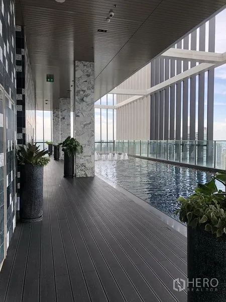 Condominium for rent in Khlong Toei, Bangkok - Covered swimming pool deck with glass railing and city outlook.