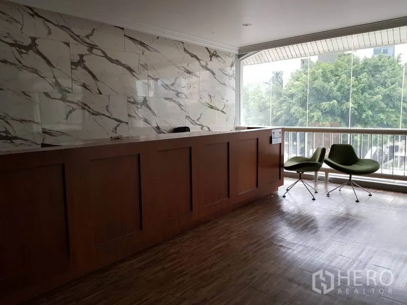 零售空间 出租在Khlong Toei, Bangkok - 木质接待台与大理石墙，旁有休闲椅与大窗树景。