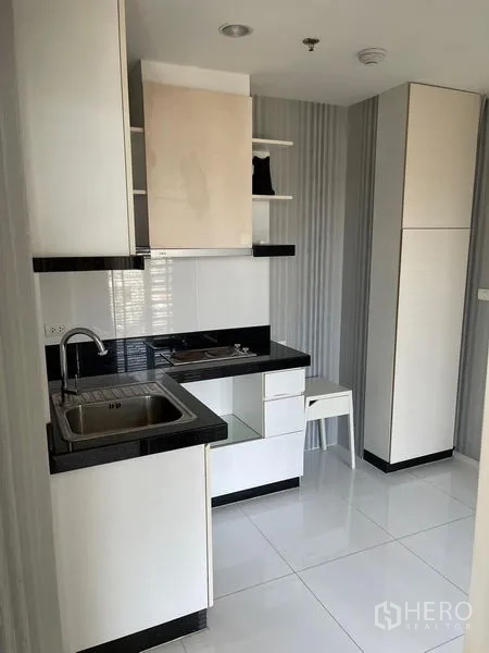 Condominium for sale in Suan Luang, Bangkok - Compact modern kitchen with white cabinetry, black countertop, sink and cooktop.