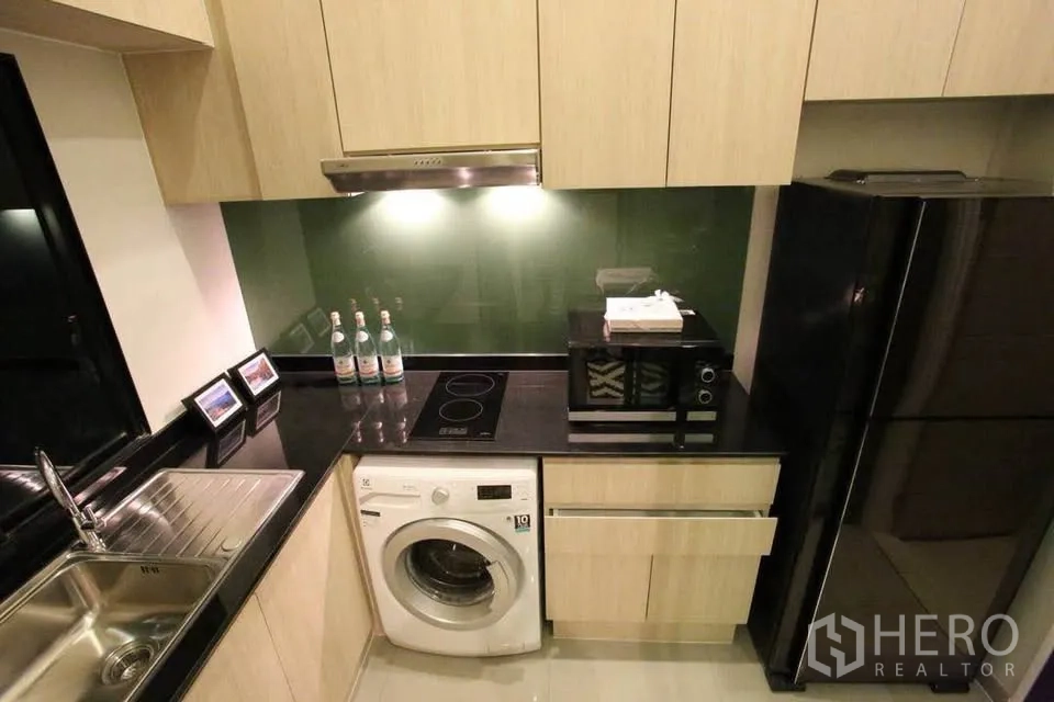 Townhouse for rent in Suan Luang, Bangkok - Modern L-shaped kitchen with black granite counters, induction cooktop, washing machine and tall fridge.