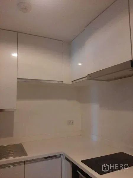 Condominium for rent or sale in Huai Khwang, Bangkok - Compact white kitchen with glossy cabinets, induction hob and extractor hood.