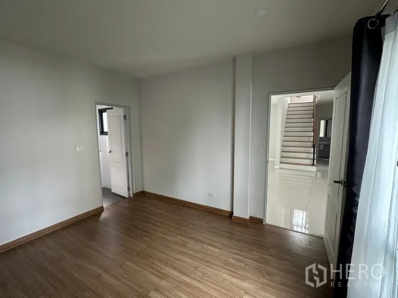 Detached House for sale in Nonthaburi - Ground-floor bedroom with wood floors and direct access to a bathroom.