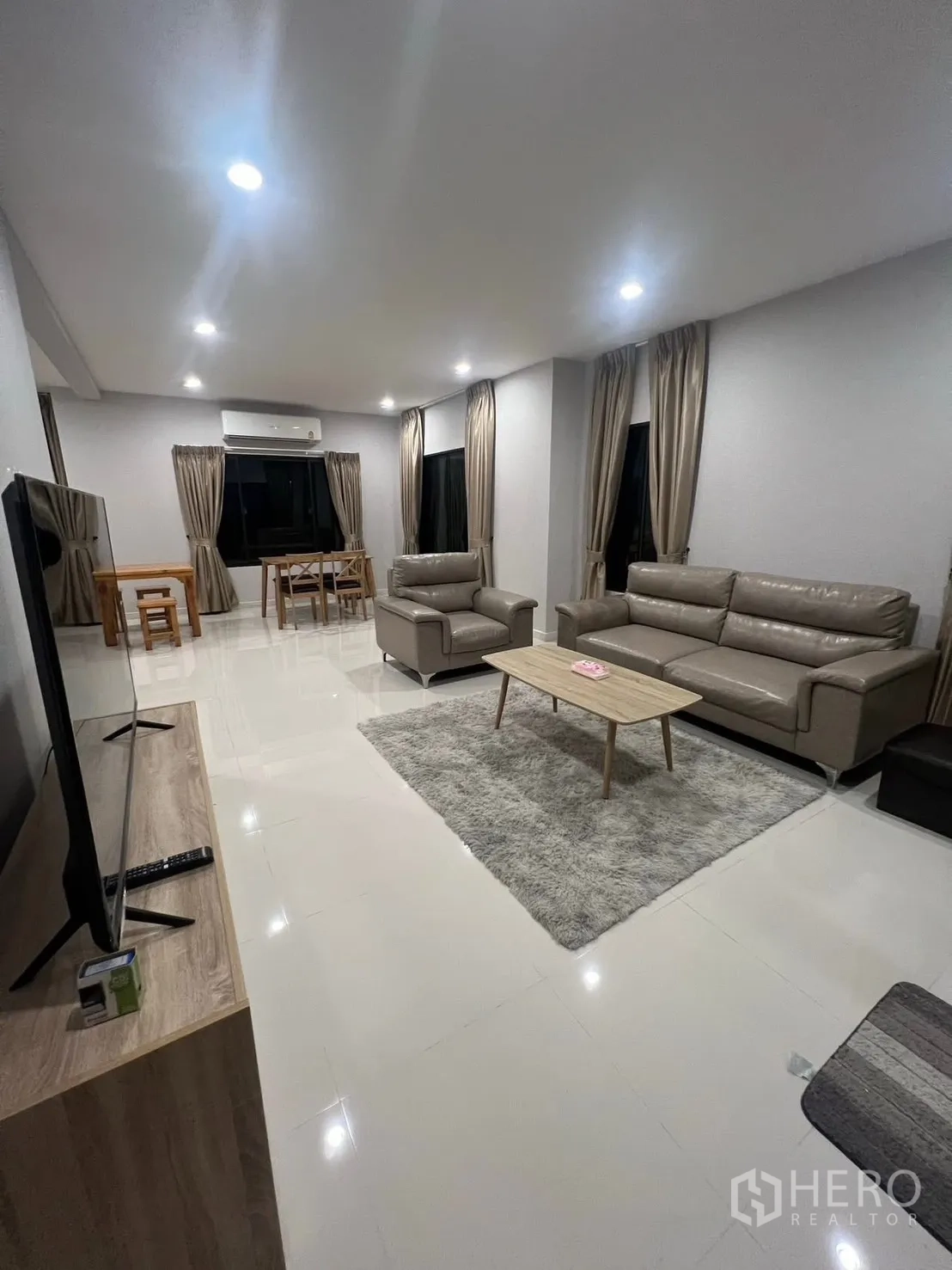 Detached House for rent in Bang Phli, Samut Prakan - Open-plan living and dining area with sofas, rug, TV and recessed lighting at night.