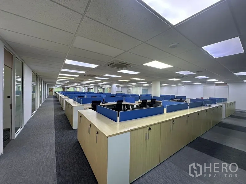 Office Space for rent - Long row of cubicles with overhead lighting and built-in storage cabinets along the aisle.