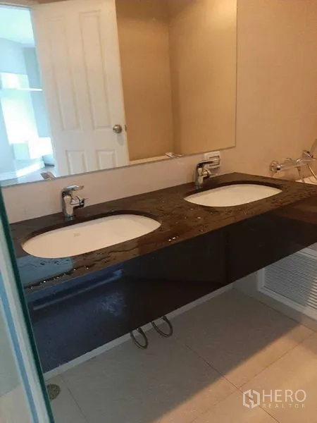 Condominium for rent or sale in Huai Khwang, Bangkok - Bathroom with double sinks on dark stone countertop and a large wall mirror