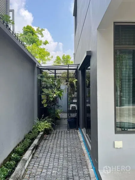 Townhouse for rent in Saphan Sung, Bangkok - Narrow side yard beside the townhouse featuring a cobblestone walkway, vertical greenery and a metal pergola.