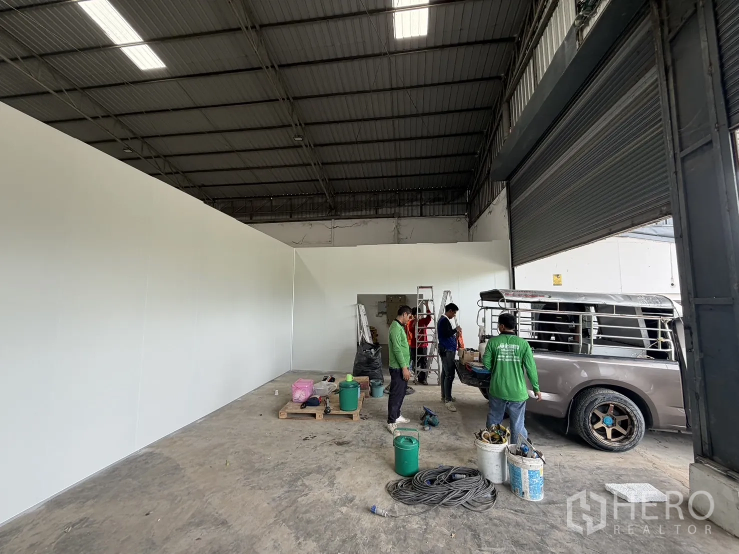 Warehouse for rent in Khlong Luang, Pathum Thani - Entrance zone featuring panel wall sections and a large roller shutter beside a parked pickup.