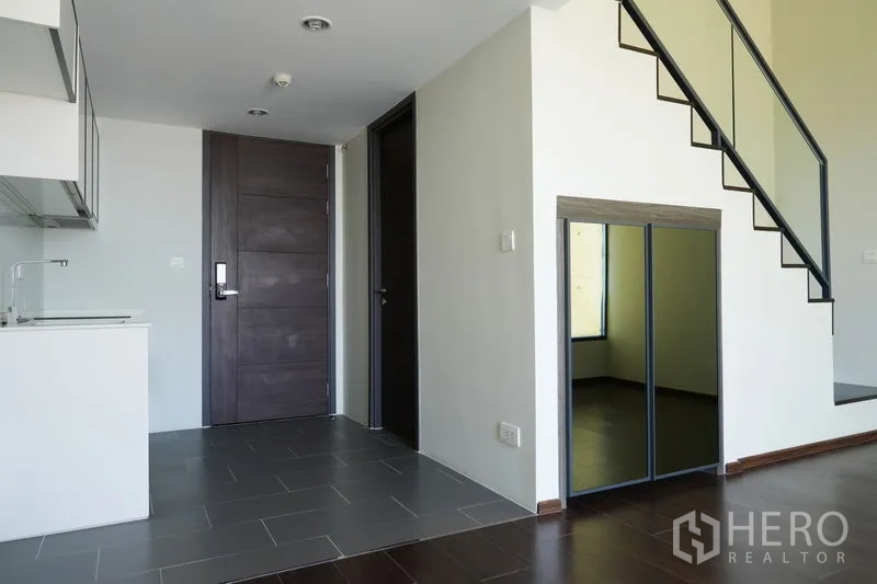 Condominium for sale in Watthana, Bangkok - Entry hall showing kitchenette, staircase with glass railing and mirrored storage under the stairs.