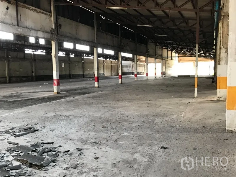 Land for rent in Phra Pradaeng, Samut Prakan - Long open shed with rows of columns and rough concrete flooring inside the complex.