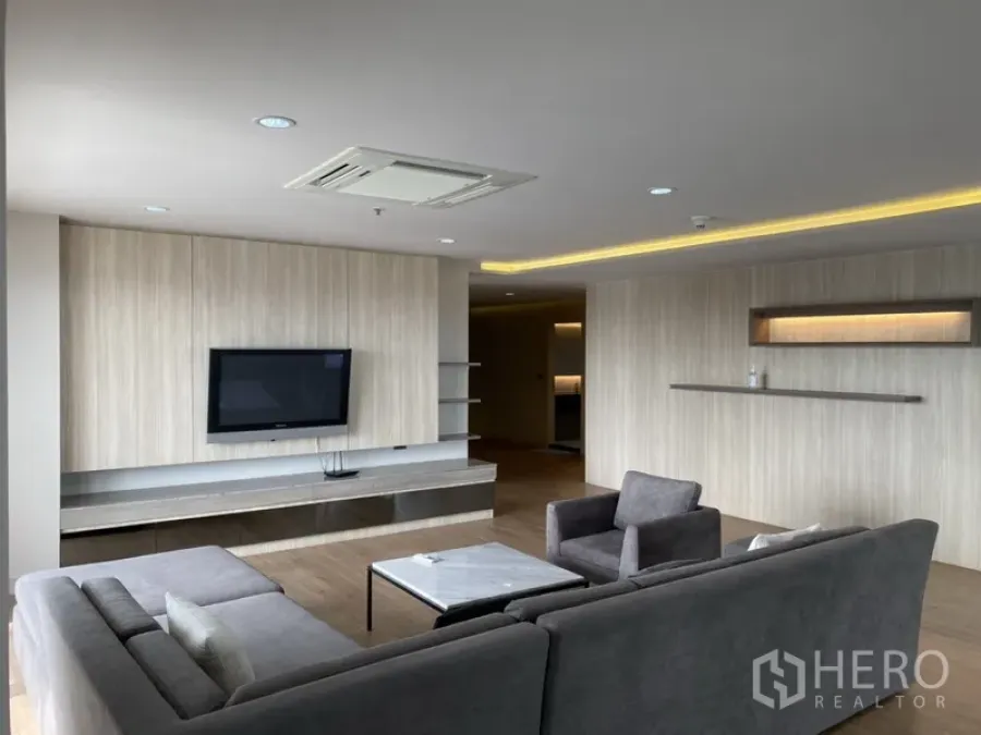 公寓 出租在Bang Rak, Bangkok - 宽敞客厅配灰色转角沙发、木质电视墙与灯带吊顶。