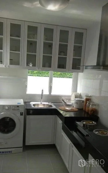 Detached House for rent in Bang Bo, Samut Prakan - Compact white kitchen with black countertops, hob, hood and washing machine.