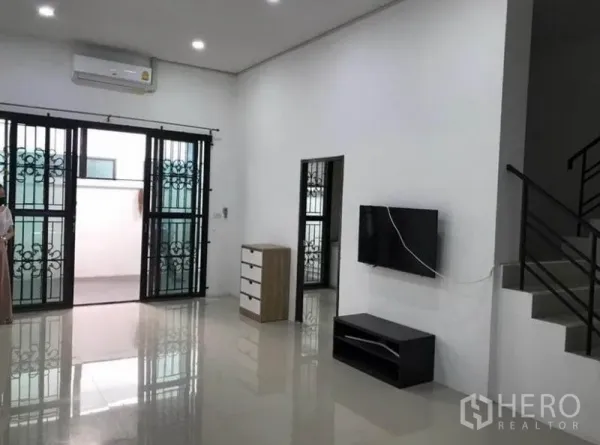 Townhouse for rent in Wang Thonglang, Bangkok - Spacious living room with air conditioner, TV console, and sliding doors.