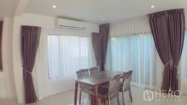 Detached House for rent in Suan Luang, Bangkok - Corner dining area with a four-seat wooden table, air conditioning, and full-height windows with curtains.