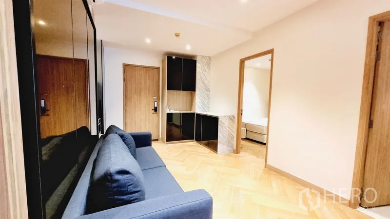 Condominium for sale in Watthana, Bangkok - Entry lounge with sofa, glossy storage cabinets and doorways to bedrooms and bathroom.