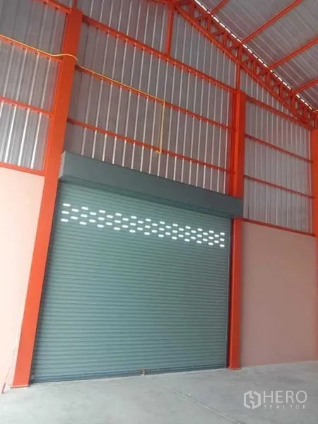 Warehouse for rent in Pathum Thani - Large metal roller shutter and orange steel frame at the warehouse entrance.