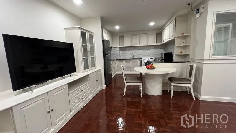 Apartment for rent in Watthana, Bangkok - Open-plan living area featuring TV cabinet, round dining table and white kitchen with marble backsplash.