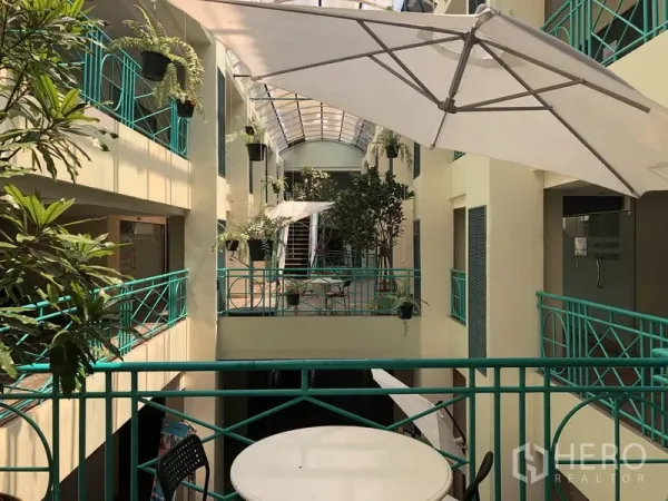 零售空间 出租在Khlong Toei, Bangkok - 采光充足的室内中庭，绿色栏杆、绿植和咖啡伞，位于店铺外。