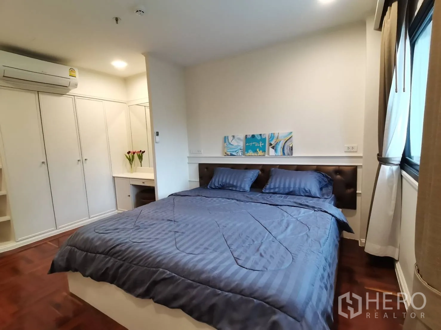 Condominium for rent in Watthana, Bangkok - Bedroom angle showing bed, built-in wardrobes, vanity desk, air conditioner, and curtained window.