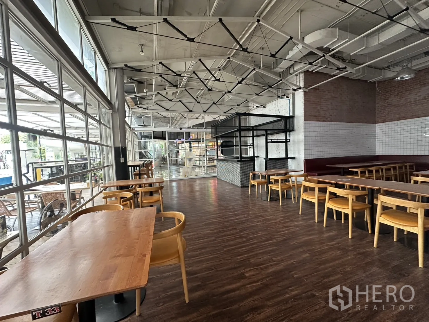 零售空间 for rent in Watthana, Bangkok - 开放式室内空间，大窗与木纹地面，配有成套桌椅。