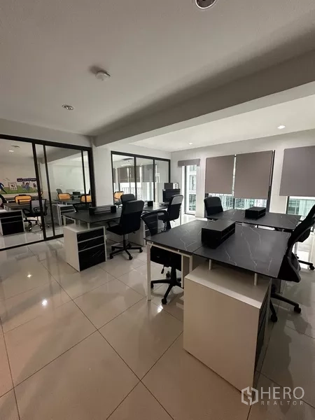 Home Office for rent - Open-plan work area with modern desks and blinds next to a glass meeting room.
