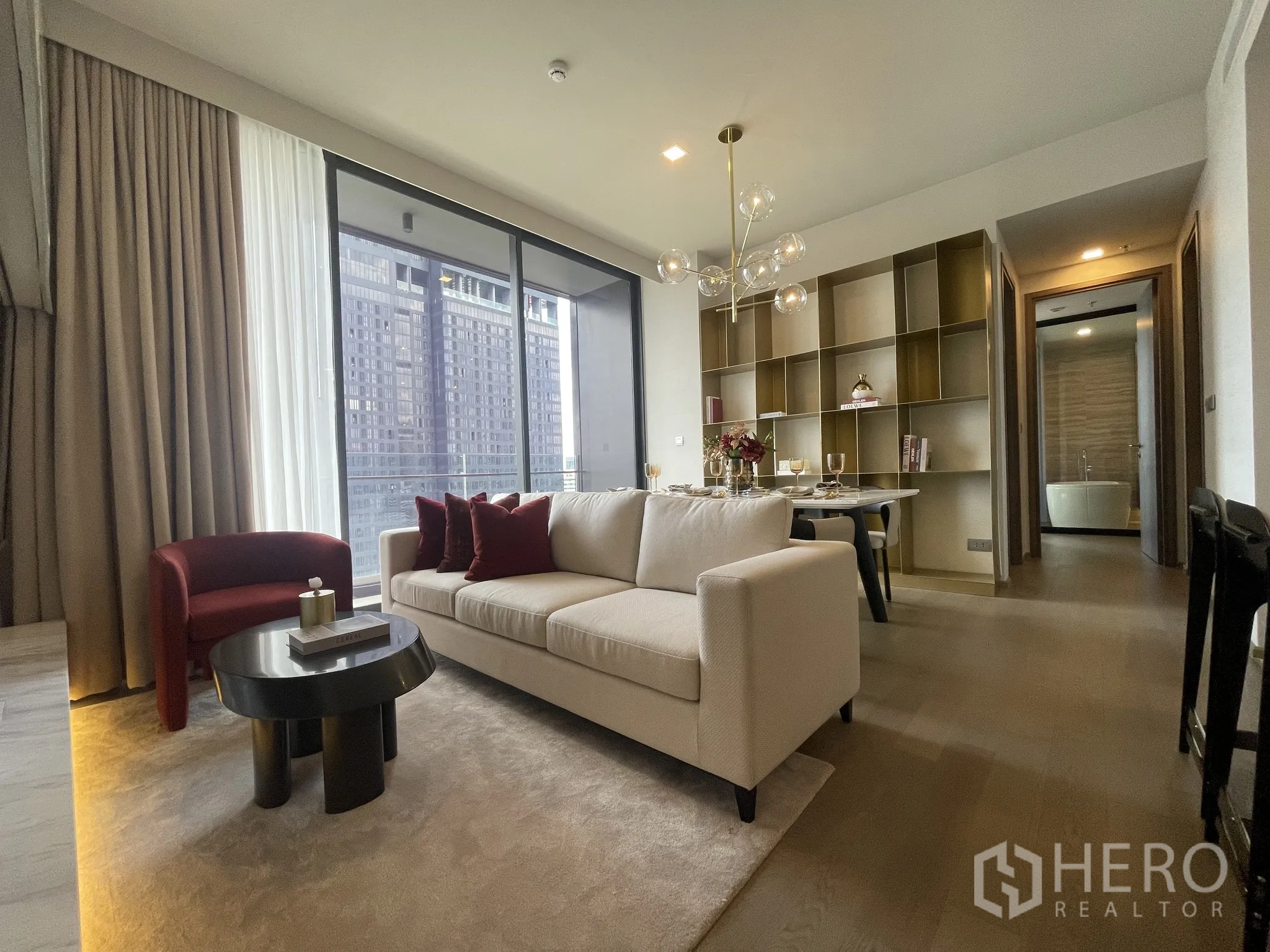 Condominium for rent in Watthana, Bangkok - Stylish living and dining area with sofa, round table, chandelier, and a balcony city view.