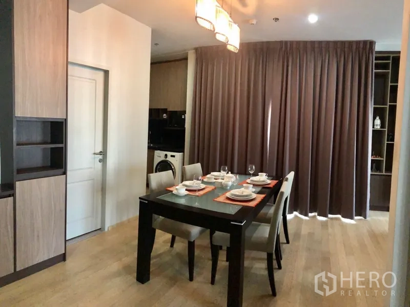 公寓 出租或出售在Bangkok - 餐区设四人餐桌与吊灯，木地板，旁有洗衣机的家务角。