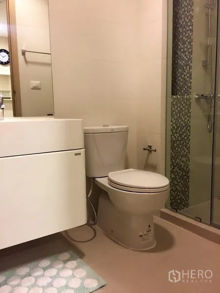 Condominium for sale in Huai Khwang, Bangkok - Modern bathroom with floating vanity, toilet, and glass-enclosed shower with mosaic tile.
